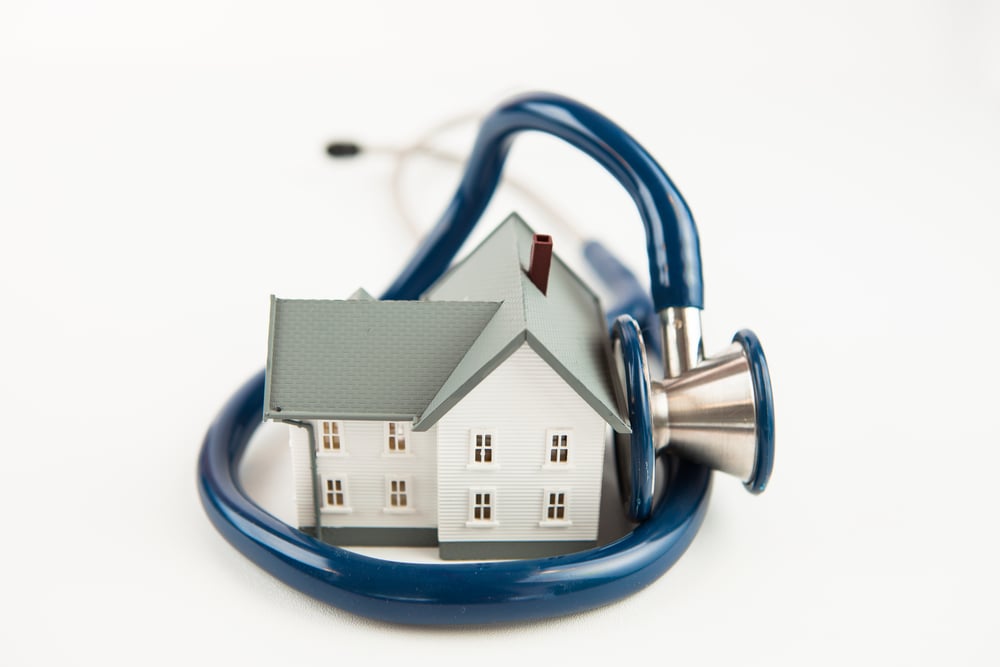 Blaues Stethoskop um kleines Hausmodell gewickelt und auf weißem Hintergrund